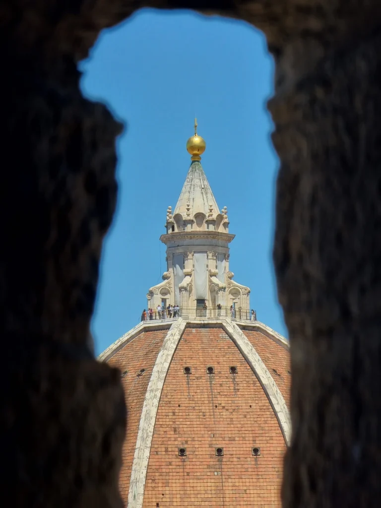 Vista della cupola del Duomo di Firenze e della lanterna con sfera dorata, incorniciata da un'apertura in pietra del Campanile di Giotto